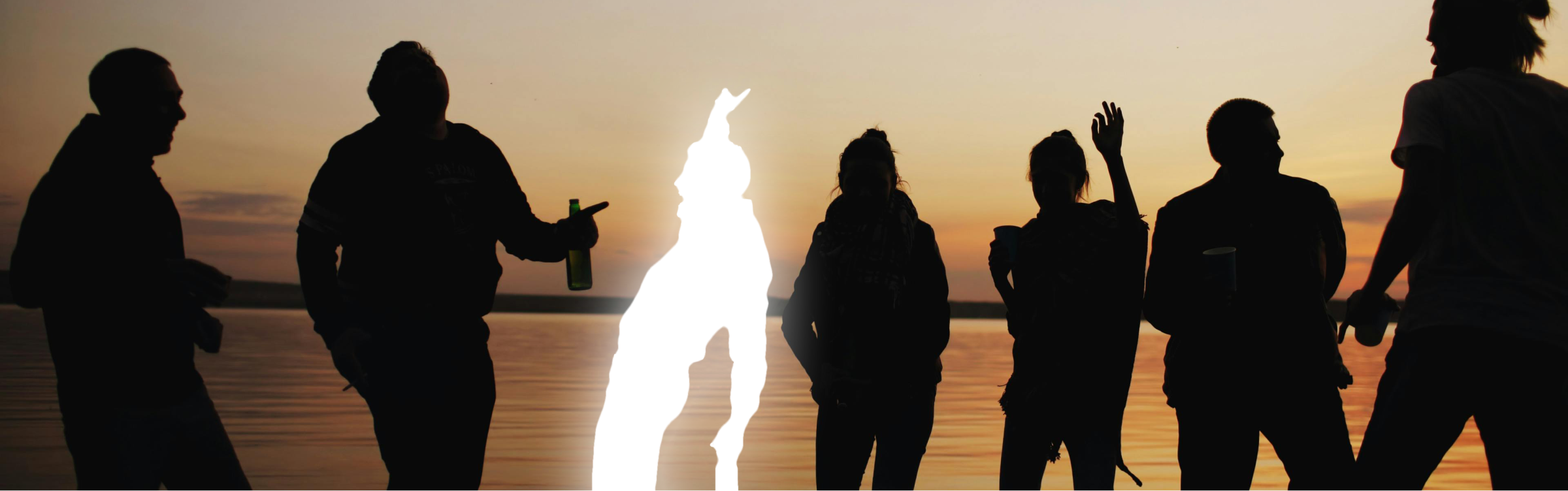 Silhouettes of friends celebrating at sunset by the water — one person glowing brightly, standing out from the crowd